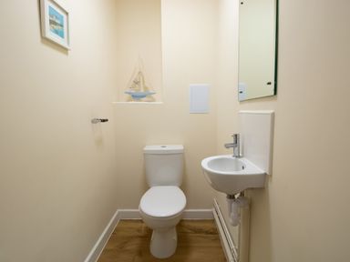 A small bathroom with a toilet and a wall-mounted sink with a mirror above it at The Ferns in Weymouth