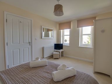 A bedroom with a bed with rolled towels a white door a small table with a television two windows and a white wardrobe at The Ferns in Weymouth
