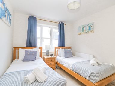 A bedroom with two single beds a bedside table lamp and window at The Ferns in Weymouth