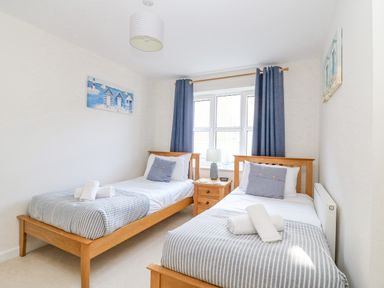 A bedroom with two single beds bedside table and window with curtains at The Ferns in Weymouth