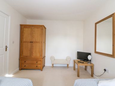 A bedroom with a wooden wardrobe a small bench a wooden table with a tv and mirror at The Ferns in Weymouth