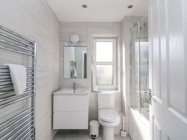 A bathroom with a white vanity sink, toilet, towel rack with towel, window, and shower area at The Ferns in Weymouth