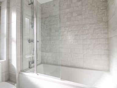 A bathroom with a bathtub shower combination and tiled walls at The Ferns in Weymouth