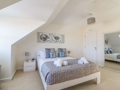 A bedroom with a double bed with gray bedding and pillows two bedside tables with lamps a large wall mirror and a floral painting at The Ferns in Weymouth