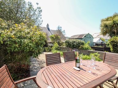 An outdoor patio with a wooden table and chairs a bottle and glasses on the table and surrounding greenery at Firkin Cottage Brewers Quay Harbour