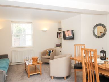 A living room with chairs a dining table and a wall mounted tv at Firkin Cottage Brewers Quay Harbour