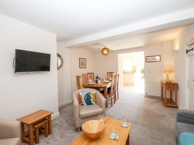 A living room with a mounted television a dining table with chairs and a wooden coffee table at Firkin Cottage Brewers Quay Harbour