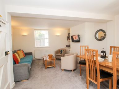 A living room with a gray sofa with colorful cushions two beige armchairs a wooden coffee table and a wooden dining table with four chairs at Firkin Cottage in Brewers Quay Harbour