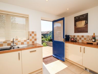 A kitchen with countertop and sink next to an open blue door and a cappuccino wall sign at Firkin Cottage Brewers Quay Harbour