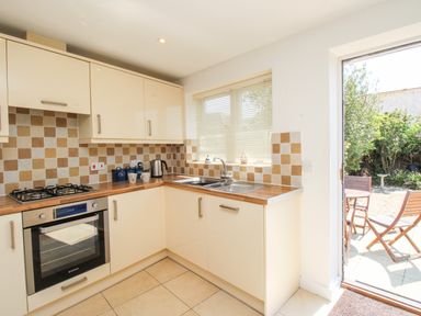 A kitchen with cream cabinets a wooden countertop a stainless steel oven a sink and a door leading to a garden at Firkin Cottage Brewers Quay Harbour