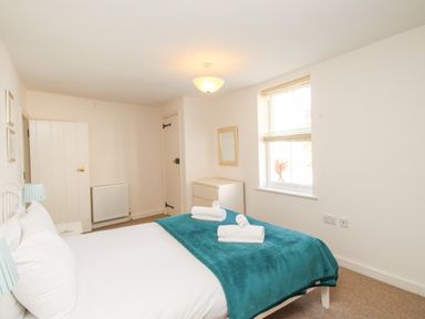 A bedroom with a bed covered in white linens and a teal blanket with two rolled towels on top at Firkin Cottage Brewers Quay Harbour