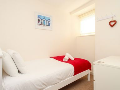 A small bedroom with a single bed with white sheets and a red blanket and a dresser near a window at Firkin Cottage Brewers Quay Harbour