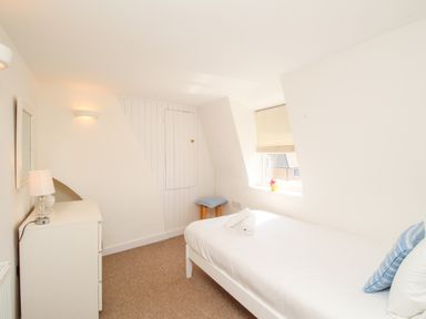 A bedroom with a single bed a dresser lamp a stool and a window at Firkin Cottage in Brewers Quay Harbour