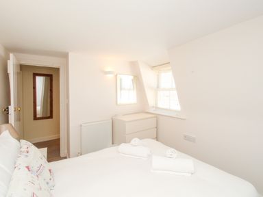 A bedroom with a bed with pillows and towels a chest of drawers a window and a door at Firkin Cottage Brewers Quay Harbour