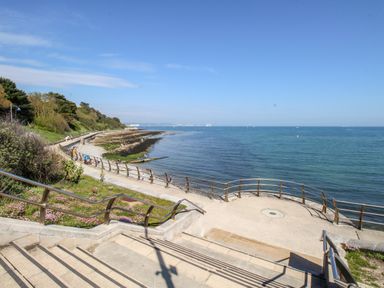 A seaside walkway with railings leading to a pebbled shore and ocean at Firkin Cottage in Brewers Quay Harbour