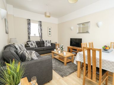 A living room with gray sofas a wooden coffee table a TV on a wooden stand and a dining table with wooden chairs at Footprint in Brewers Quay Harbour