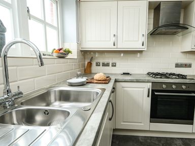 A kitchen with a stainless steel sink, countertop, oven, stove, white cabinets, and a bowl of fruit at Footprint in Brewers Quay Harbour