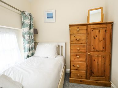 A bedroom with a single bed white bedding a wooden dresser with a mirror and a window with curtains at Footprint in Brewers Quay Harbour