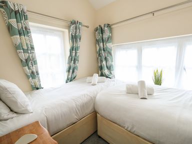 A bedroom with two single beds with white bedding and rolled towels by windows with patterned curtains at Footprint Brewers Quay Harbour