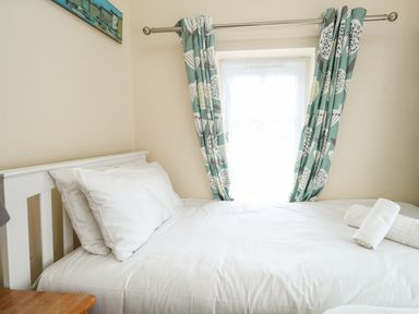 A bedroom with a white bed and pillows by a window with patterned curtains at Footprint in Brewers Quay Harbour