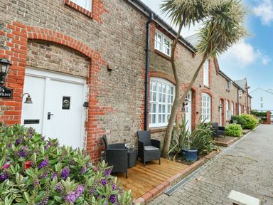 A row of brick houses with white doors and windows small patios with black chairs and potted plants along a paved path at Footprint in Brewers Quay Harbour