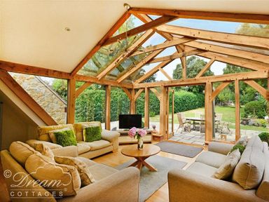 A living room with beige sofas and a round wooden table under a wooden frame glass ceiling at Fossil Barn in Weymouth