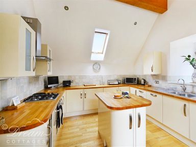 A kitchen with wooden countertops white cabinets an island a gas stove a microwave and a skylight at Fossil Barn in Weymouth