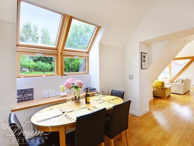 A dining area with a wooden table set for four under skylight windows and a living room visible through an arch at Fossil Barn in Weymouth