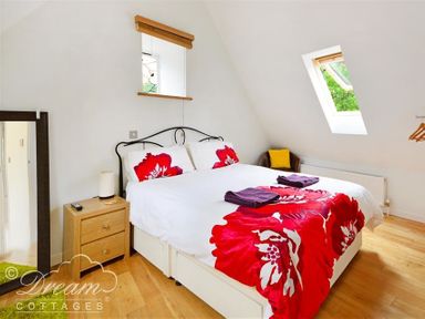 A bedroom with a double bed with red flower bedding a wooden bedside table and a tall mirror at Fossil Barn in Weymouth
