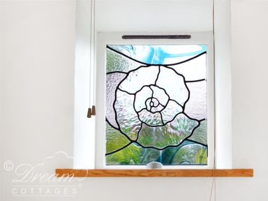 A stained glass window with a spiral shell design and a wooden windowsill at Fossil Barn in Weymouth
