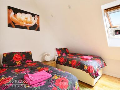 A bedroom with two single beds with floral bedding a window and a wall painting at Fossil Barn in Weymouth