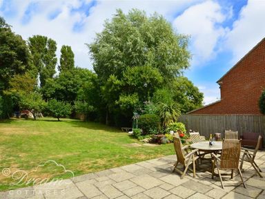A garden with a lawn trees and a patio with a wooden table and chairs at Fossil Barn in Weymouth