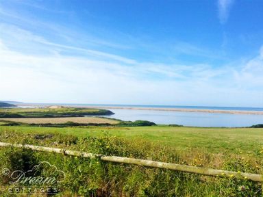 A grassy field with a wooden fence overlooking water and a sandy beach at Fossil Barn in Weymouth