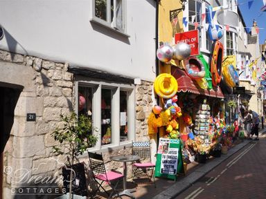 A street view with a shop selling colorful inflatable toys and a small outdoor seating area at Fossil Barn in Weymouth