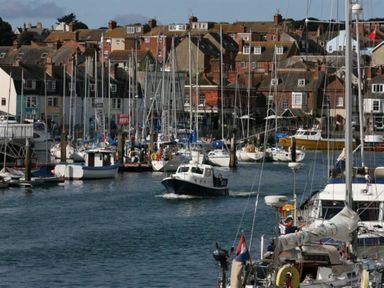 A harbor with sailboats docked and a motorboat on the water with houses in the background at Georges House Brewers Quay Harbour