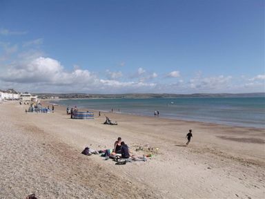 A beach with people sitting on towels and walking near the water at Georges House Brewers Quay Harbour