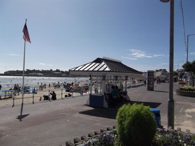 A beach with people on the sand and a shelter on the promenade at a seaside location