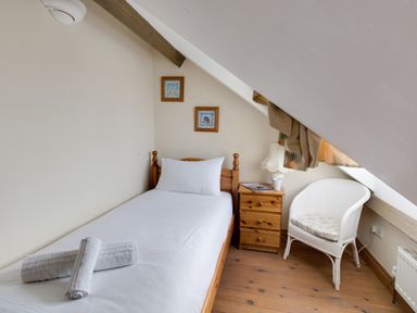 A small bedroom with a single wooden bed white bedding a wooden bedside table with a lamp a white wicker chair and two framed pictures on the wall at Georges House Brewers Quay Harbour