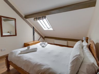 A bedroom with a wooden bed frame white bedding towels on the bed wooden chest a wall mirror and a skylight window at Georges House Brewers Quay Harbour