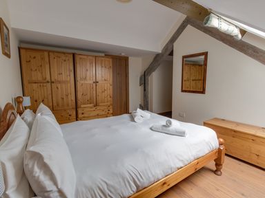 A bedroom with a wooden bed white bedding wooden wardrobes a mirror and a wooden bench at Georges House Brewers Quay Harbour