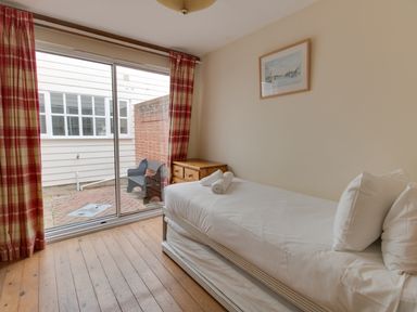 A bedroom with a single bed and rolled towels near sliding glass doors with checkered curtains at Georges House Brewers Quay Harbour