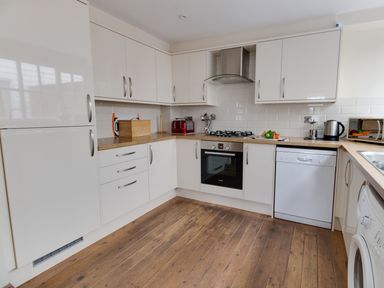 A kitchen with white cabinets wooden countertops a stove an oven a dishwasher a toaster kettle microwave and a washing machine at Georges House in Brewers Quay Harbour