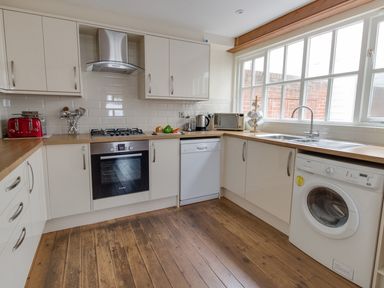 A kitchen with white cabinets wooden countertops and appliances including oven dishwasher and washing machine at Georges House in Brewers Quay Harbour