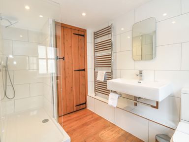 A bathroom with a walk-in shower wooden door white sink and towel radiator at Georges House Brewers Quay Harbour