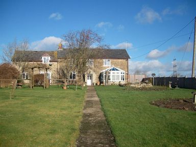 A stone house with a pathway leading to the door and a garden with trees and grass at Grazeland Cottage in Bridport