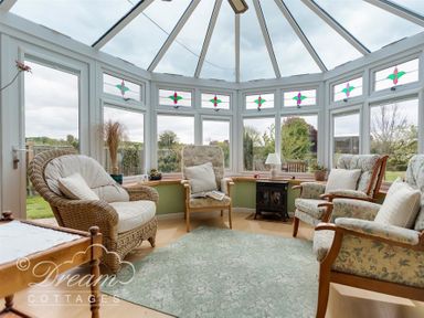 A conservatory with armchairs a wicker chair a small stove and plants at Grazeland Cottage in Bridport