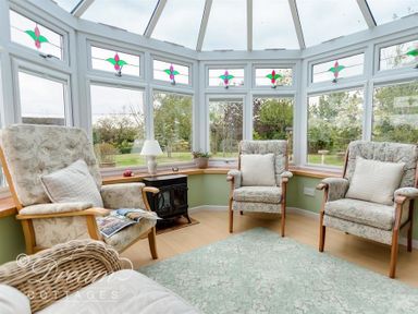 A conservatory with three armchairs a small stove a lamp and windows with stained glass at Grazeland Cottage Bridport
