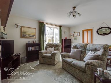 A living room with sofa armchair television and bookshelf at Grazeland Cottage in Bridport