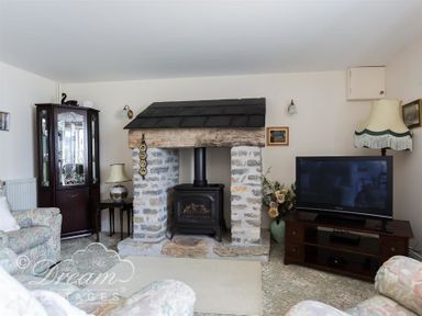 A living room with a stone fireplace TV cabinet and armchairs at Grazeland Cottage in Bridport
