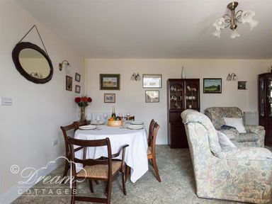 A dining area with a table set for four surrounded by chairs and floral armchairs in a room at Grazeland Cottage in Bridport